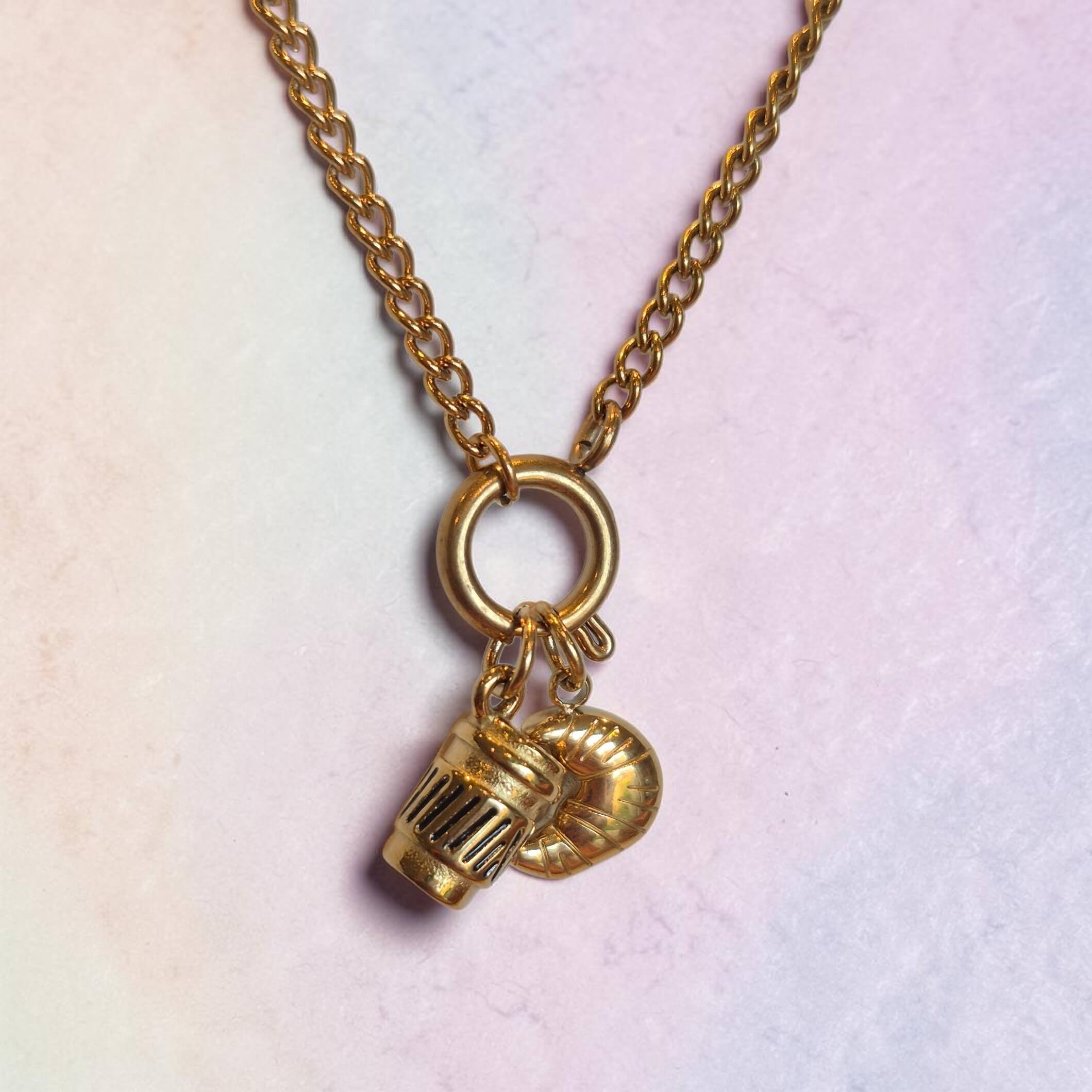 Gold necklace with two charms on a pastel background