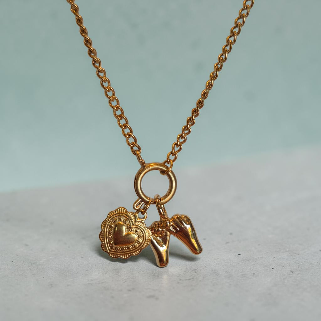Gold necklace with heart and horse shoe charm on a light gray surface